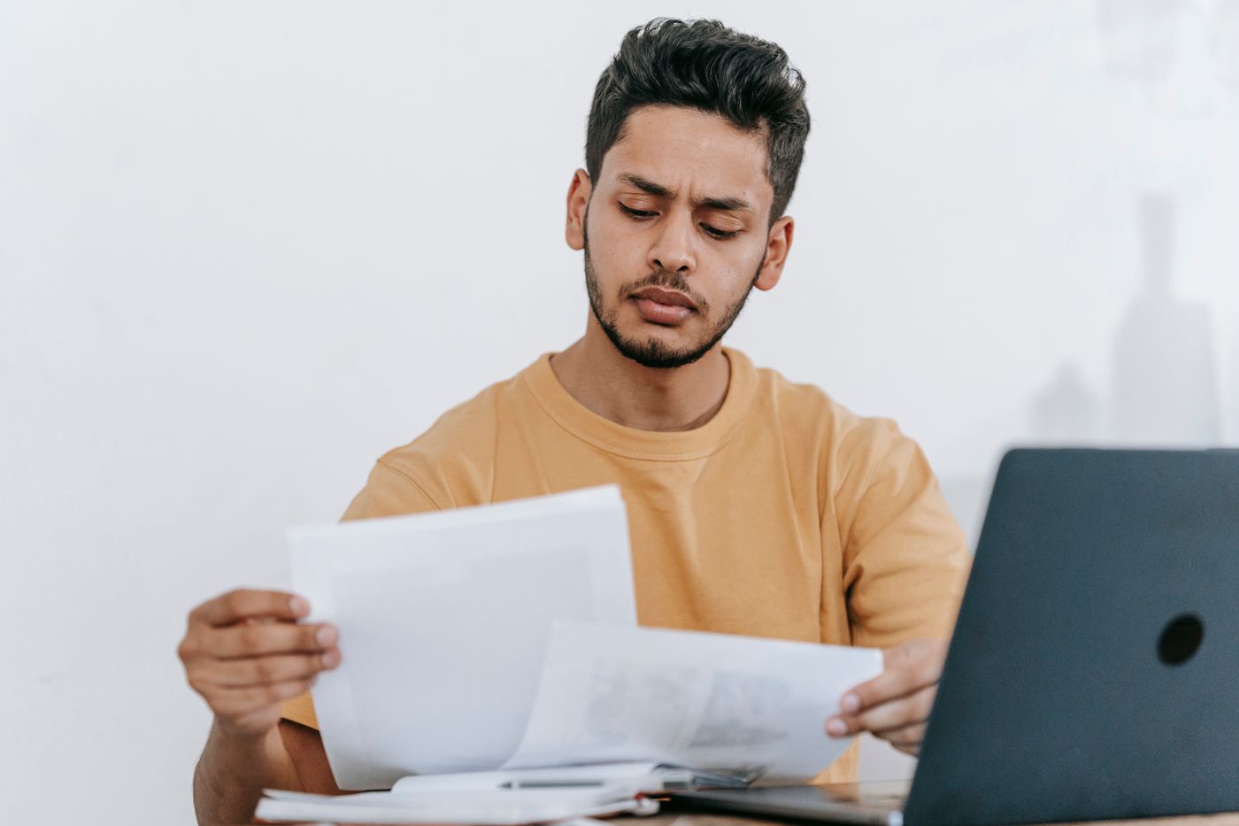 Stock photo of a man reviewing printed documents beside a laptop