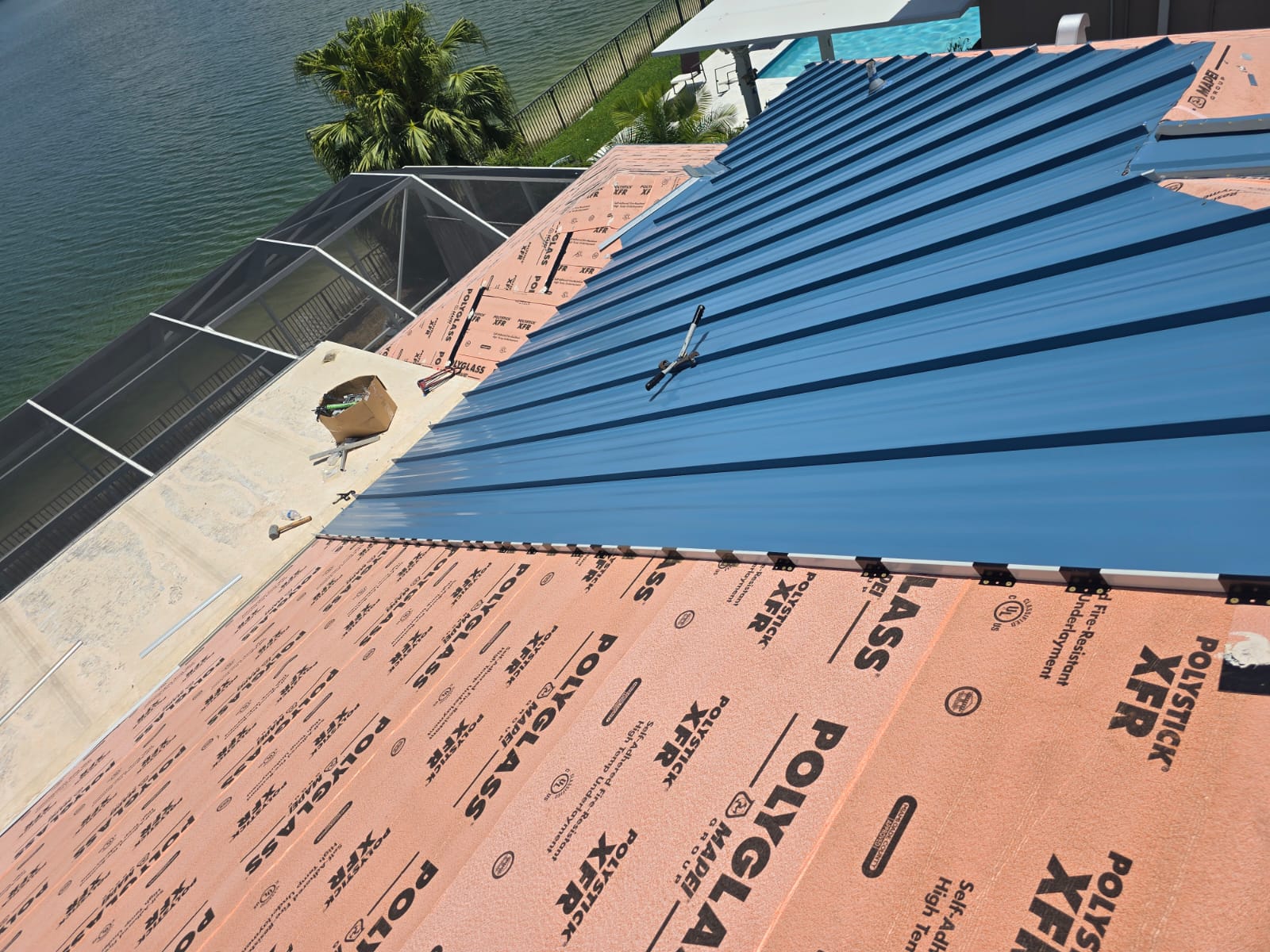 Exposed attachment clips along the edge of a blue standing-seam metal roof panel over Polystick XFR underlayment.