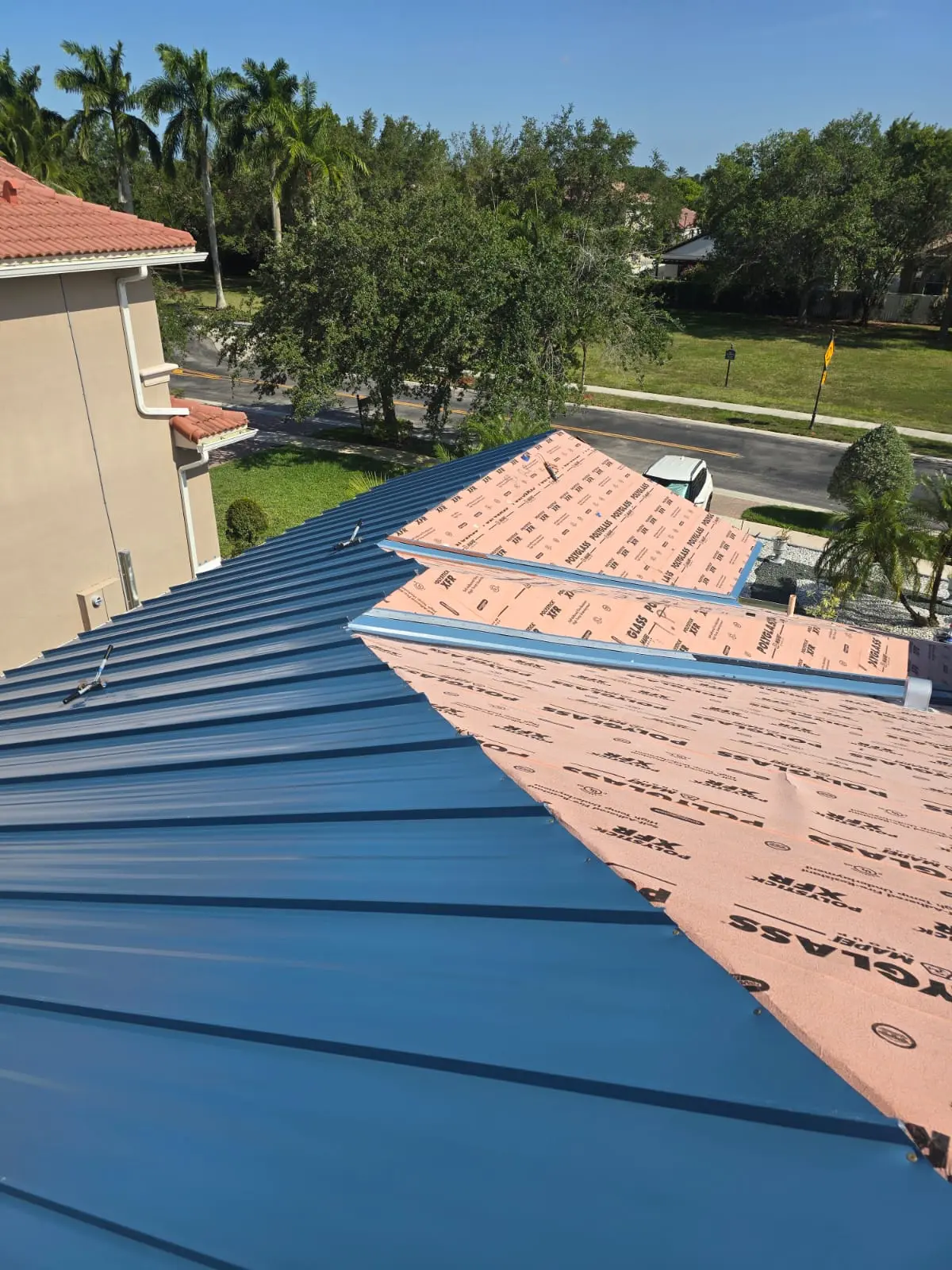 Polystick XFR underlayment beside installed Regal Blue standing-seam panels during a Miramar tile-to-metal roof conversion.