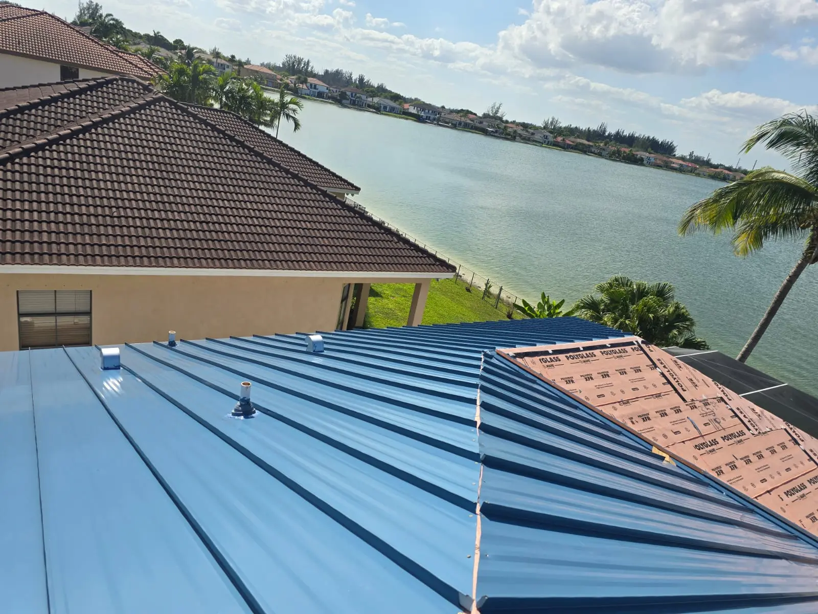 Regal Blue standing-seam panels beside exposed Polystick XFR underlayment during installation on a Miramar home.