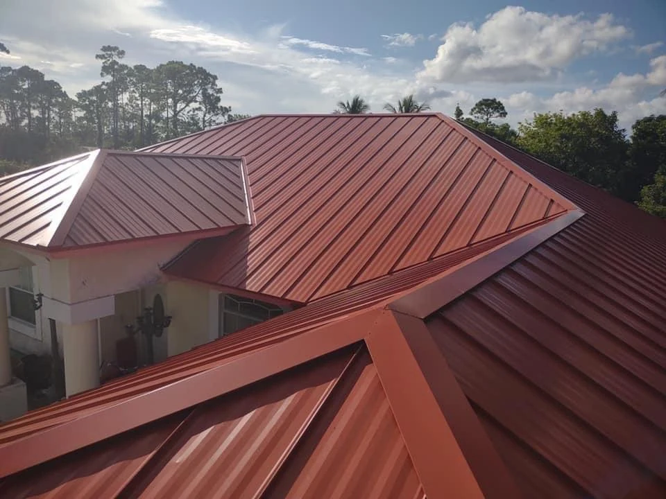 Red metal roof panels across intersecting roof sections, with matching hip and ridge caps.