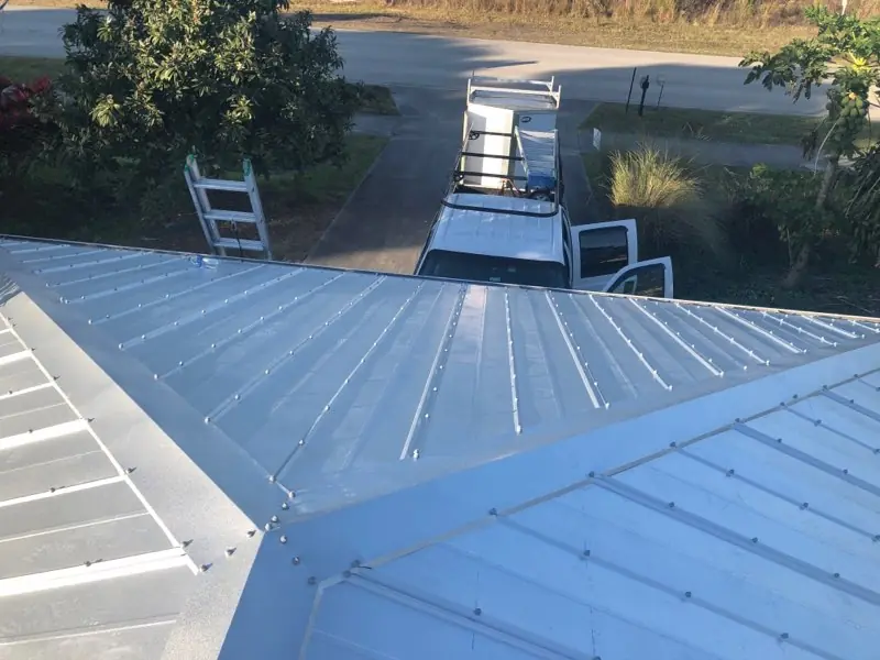 White exposed-fastener metal roof panels and valley flashing during installation.