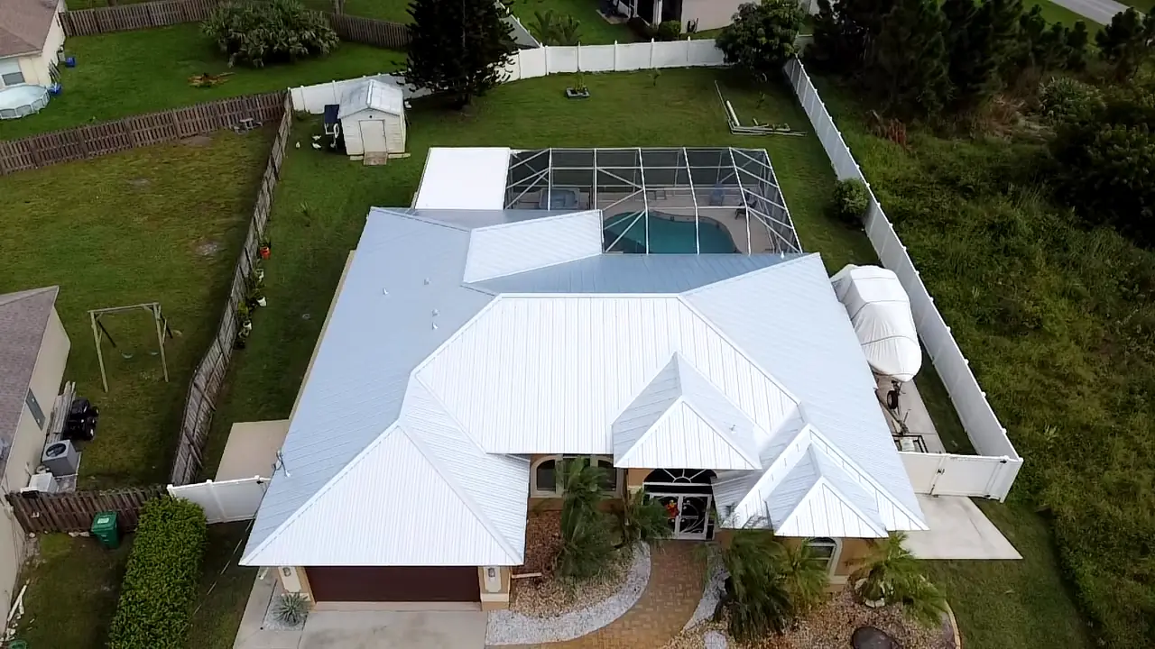 Aerial view of a white metal roof with multiple hips on a home with a screened pool