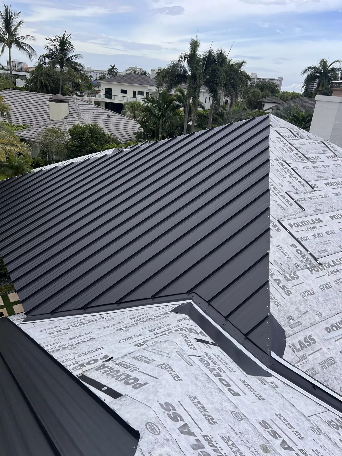 Dark standing-seam metal roof installation around two residential skylights.