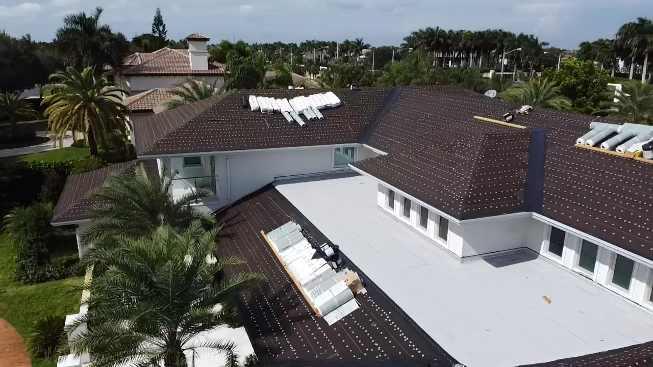 Aerial view of work underway across dark tile and adjoining low-slope roof sections.