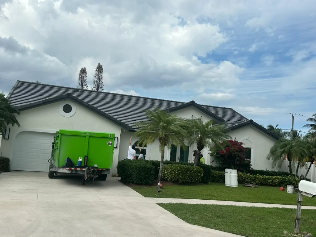Residential roofing job site with a gray flat-profile tile roof, crew members, and equipment.