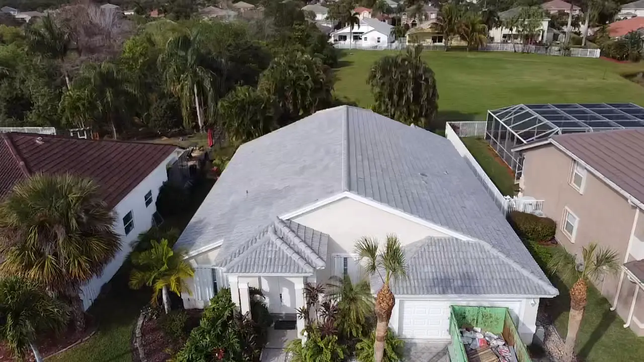Aerial view of a light gray tile roof with a roofing dumpster at the active job site.