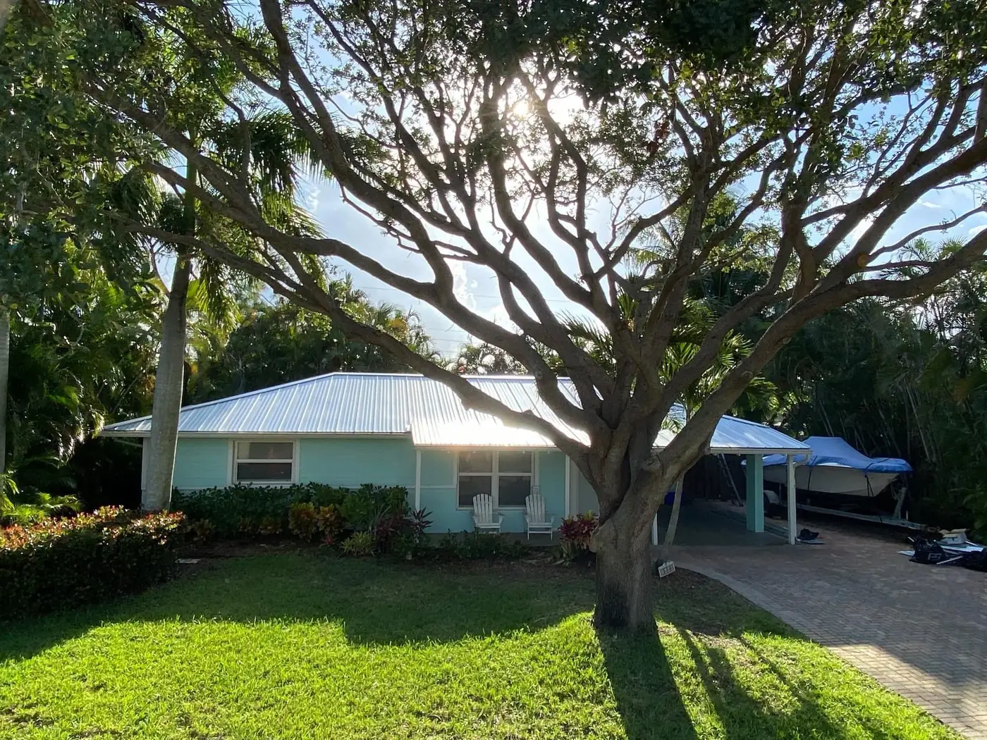 Front view of a small home with a completed white metal roof beneath a large tree.