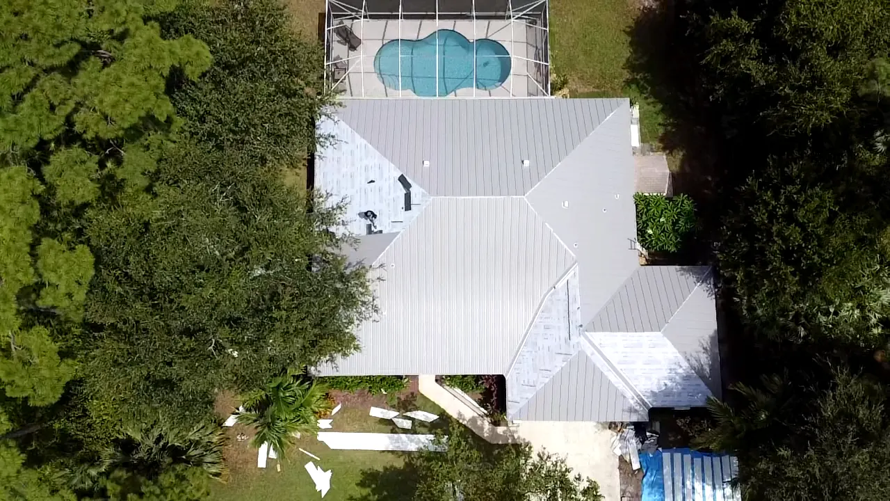 Top-down aerial view of a white metal roof with several hips beside a pool.