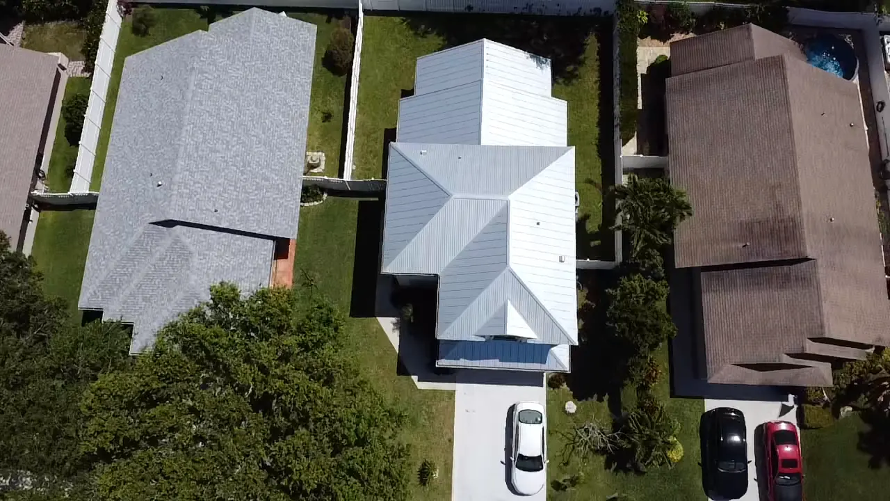 Top-down aerial view of a white metal roof between neighboring homes.