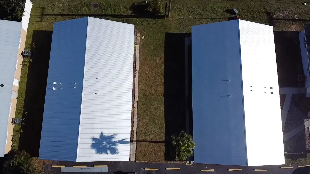 Top-down aerial view of two long buildings with completed white metal roofs.