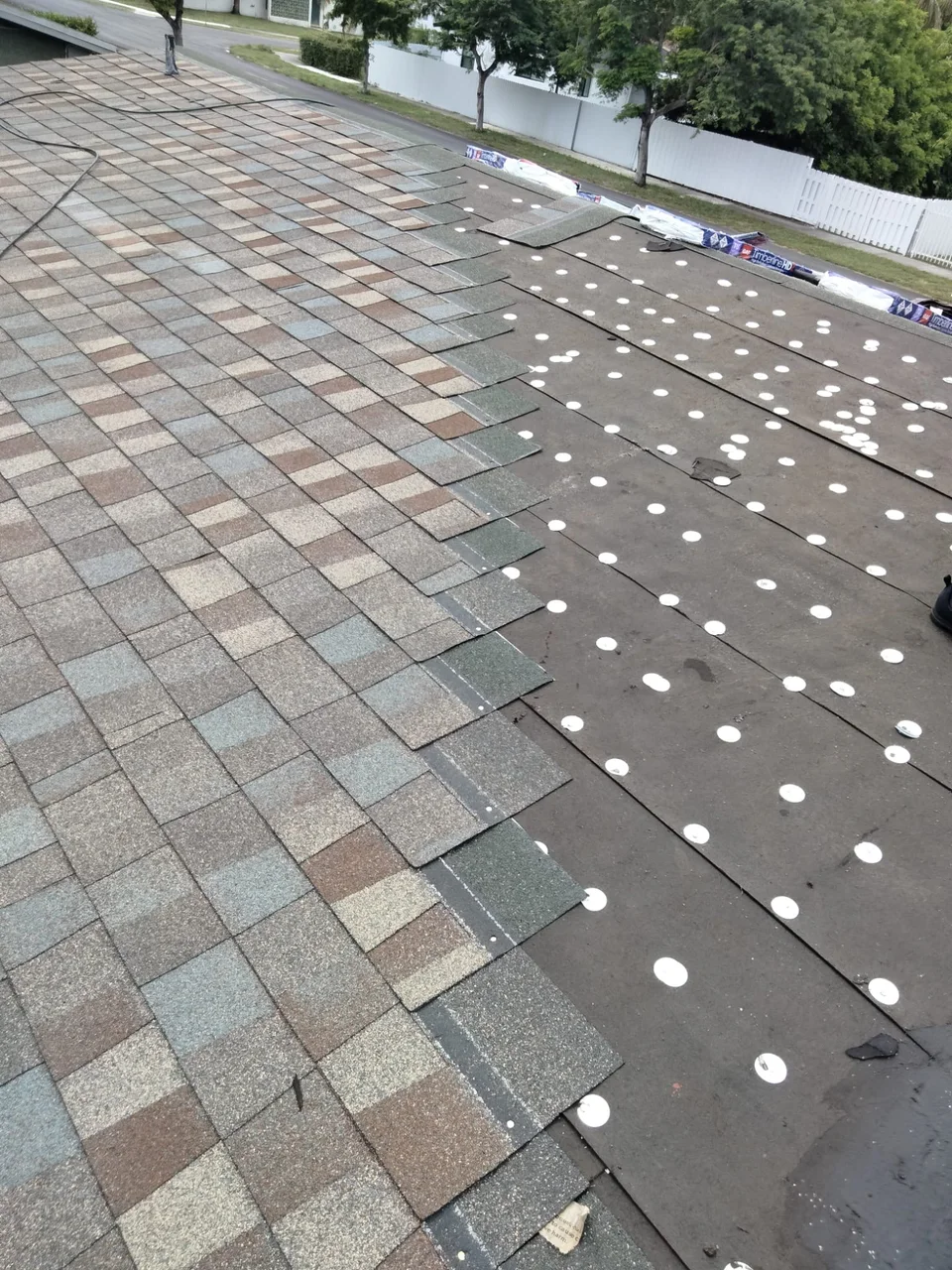 Shingles being installed beside exposed underlayment secured with round caps.