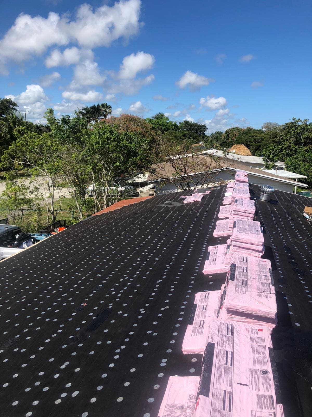 Number 30 felt dry-in on a Florida roof with dense rows of capped roofing nails and shingle bundles staged near the ridge.