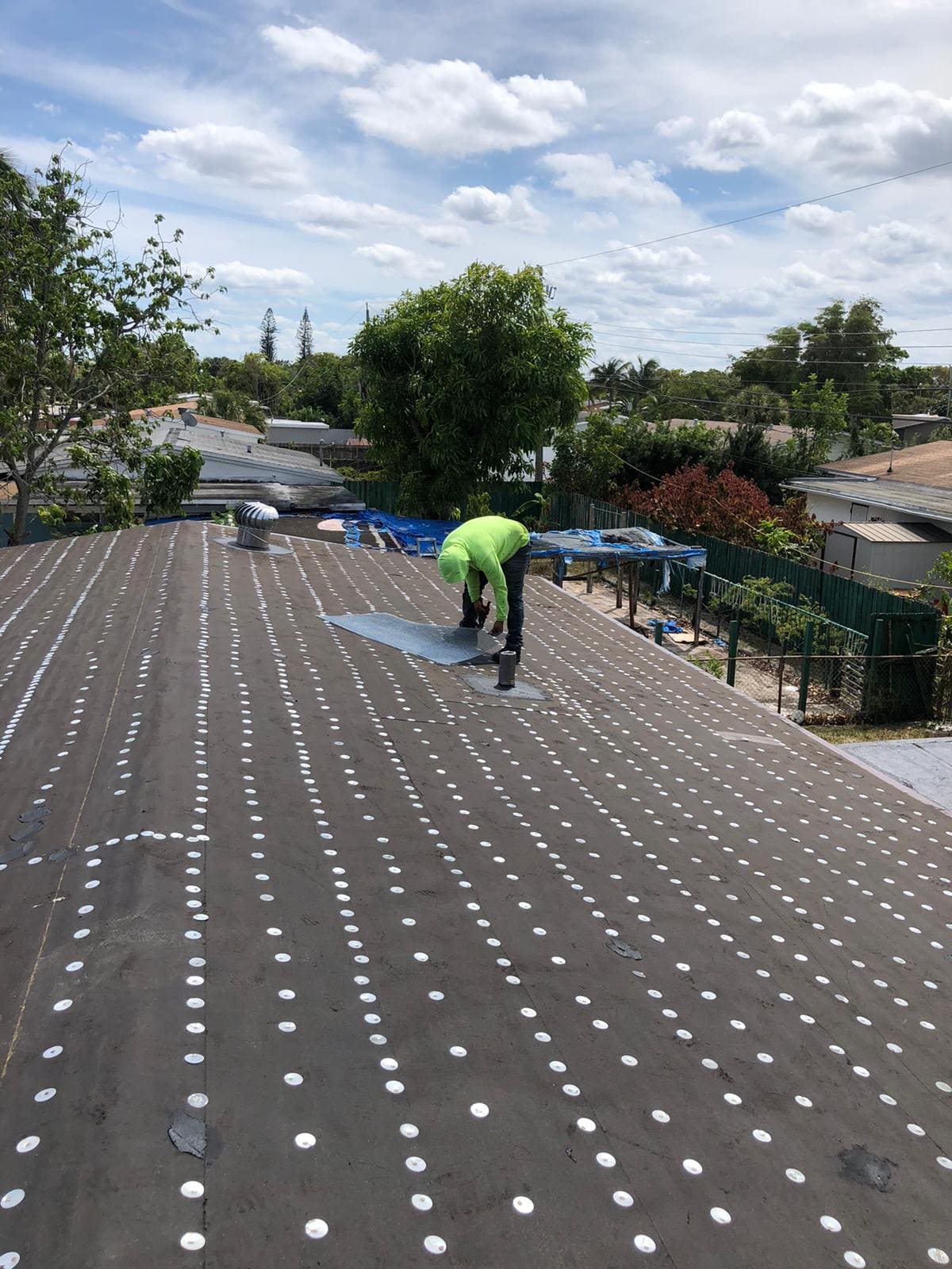 Roofer working over number 30 felt underlayment installed with rows of roofing nails and round metal tin caps.