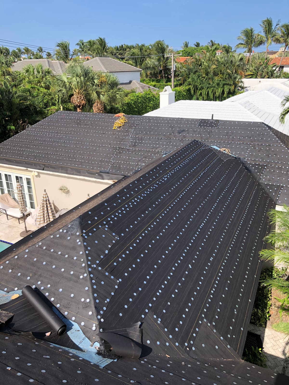 Number 30 felt underlayment installed in overlapping courses with round metal tin caps across a South Florida asphalt shingle roof.