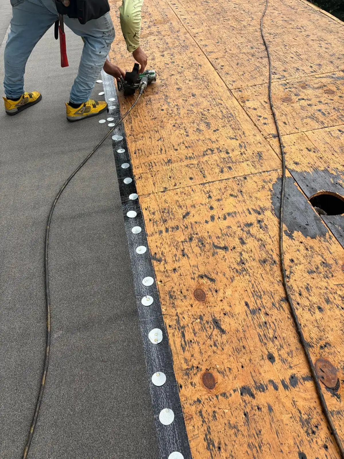 Close-up of Polystick IR-Xe shingle underlayment beside exposed plywood with metal cap fasteners along the covered sheet edge.
