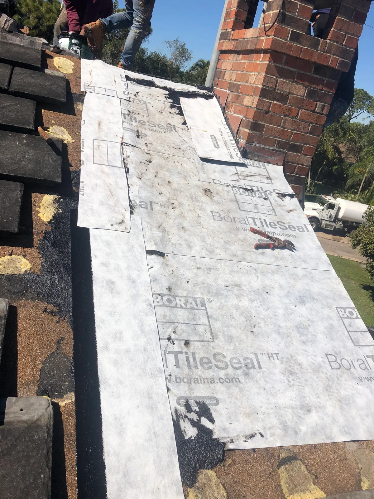 New peel-and-stick underlayment covering the repaired roof decking around the brick chimney before tiles are reinstalled.