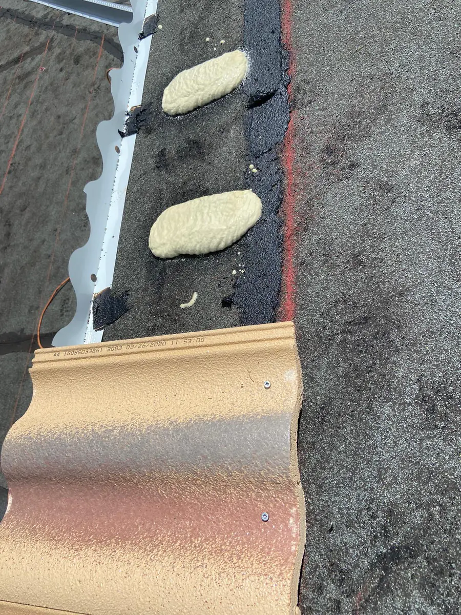 High-profile concrete roof tile beside medium foam adhesive paddies and visible fastener heads.