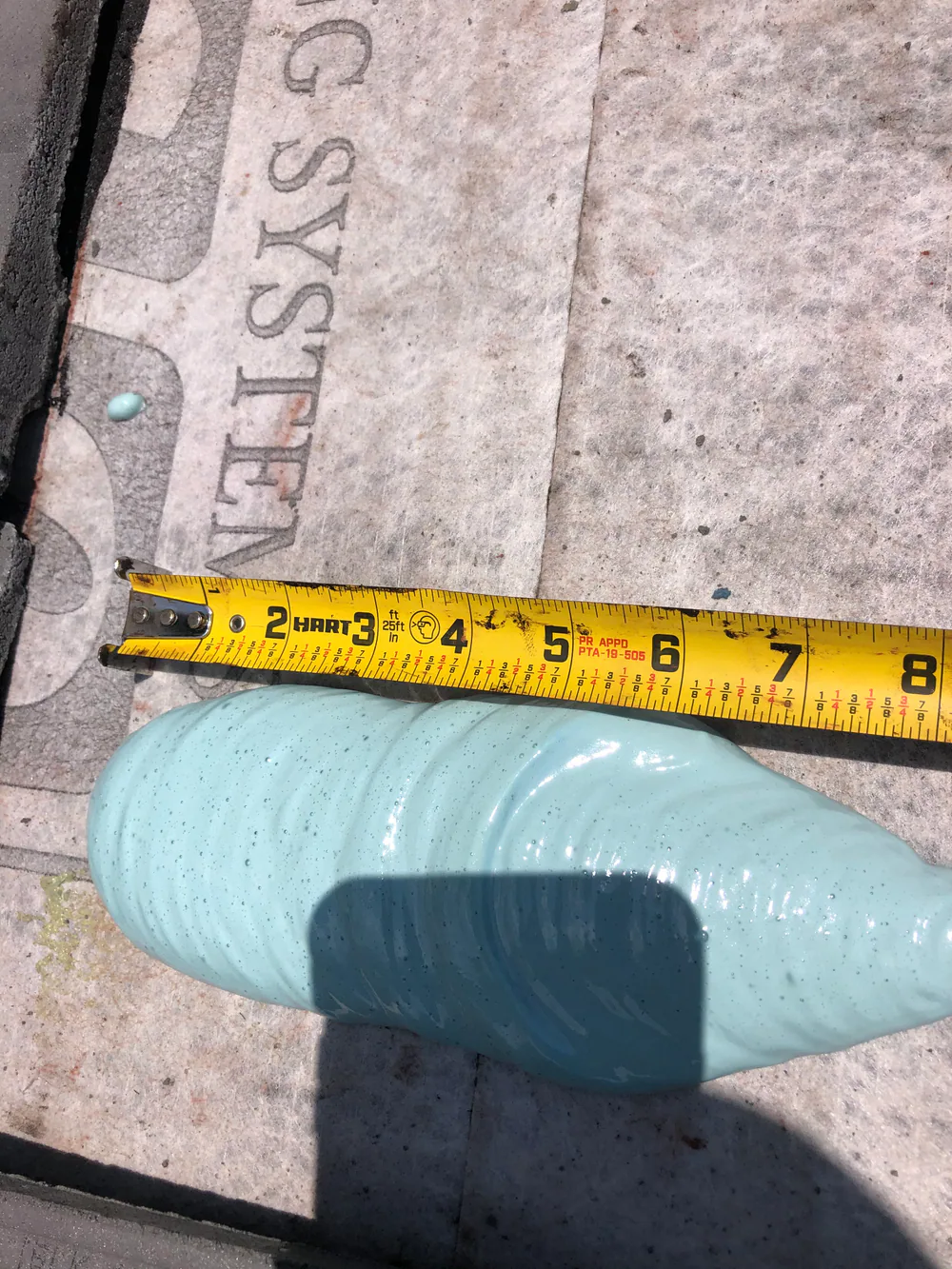 Tape measure beside a medium roof tile adhesive paddy during a field installation check.