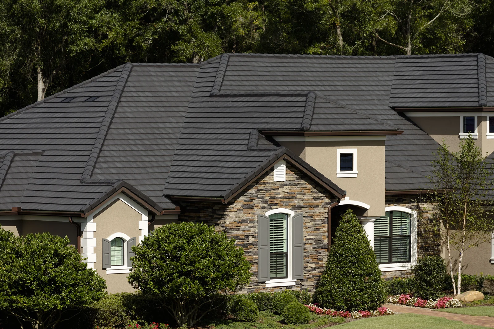 Dark gray Eagle Bel Air flat concrete roof tiles on a house with a stone and stucco exterior